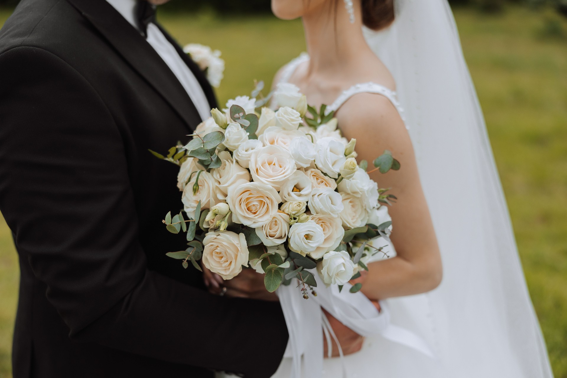 The groom hugs the bride, the bride holds a wedding bouquet. Cropped photo. Groom in a black suit. Details